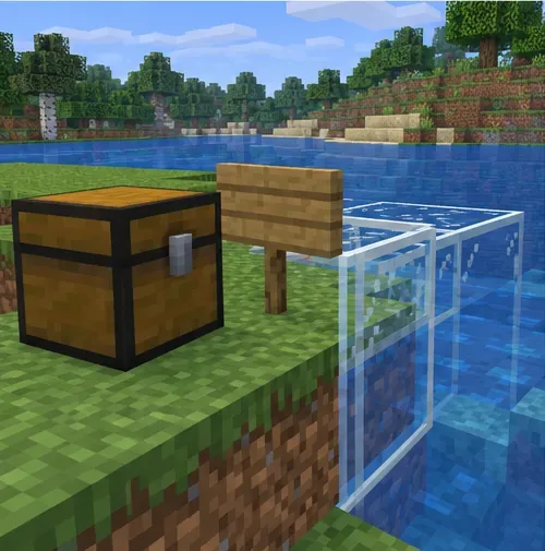 A chest, wooden sign, glass blocks, and water sit together at a grassy shoreline.