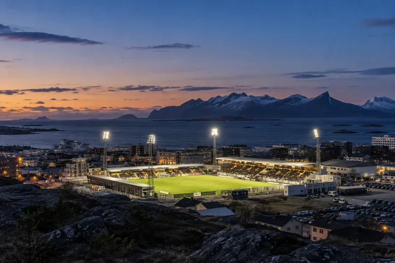 Een verlicht voetbalveld onder een berglandschap in de schemering in Noord-Noorwegen.