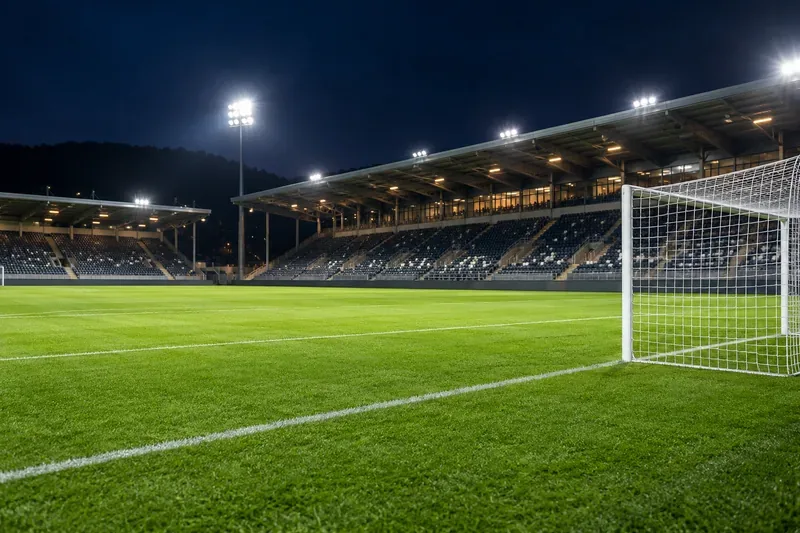Een leeg voetbaldoel en een groen veld onder de stadionverlichting 's nachts.