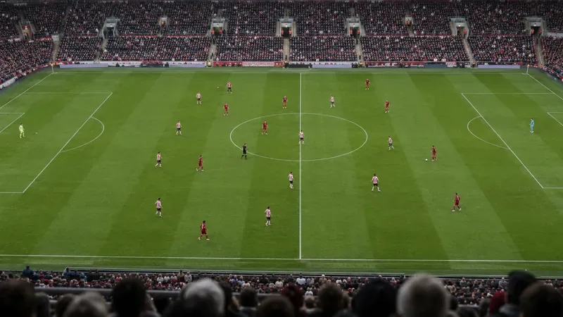 Een overzichtsfoto van twee voetbalteams in rode en rood-witte tenues die hun formatie behouden op een groen veld.