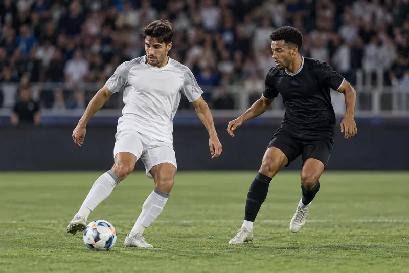 Twee voetballers zonder logo strijden om een ​​bal op een verlicht veld.