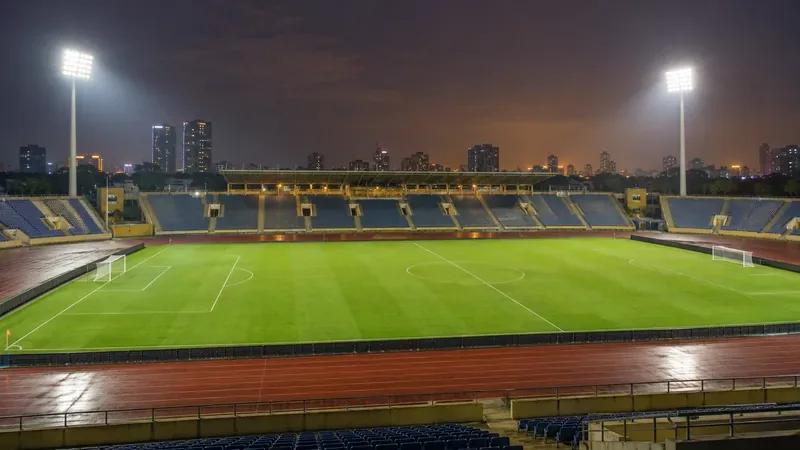 Een voetbalstadion 's nachts, verlicht door schijnwerpers, met een groen veld en lege tribunes.