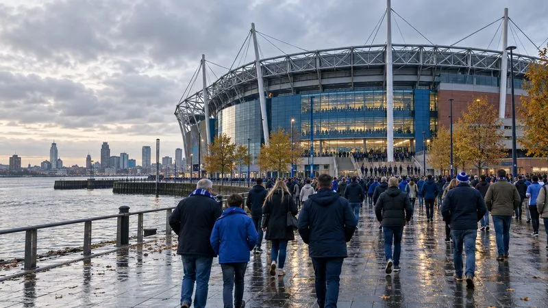 Supporters lopen onder een bewolkte herfsthemel richting een modern voetbalstadion aan het water.