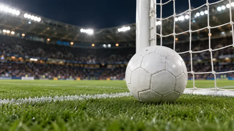 Een eenvoudige witte voetbal ligt op kort gras naast een doelnet onder de stadionverlichting.