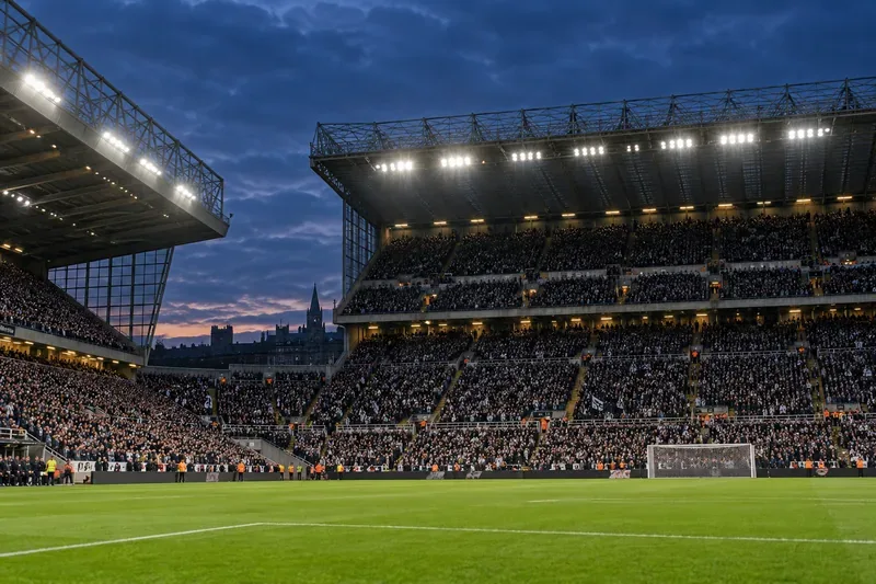 Campo da calcio illuminato a giorno, con un manto erboso verdeggiante all'ora blu e tifosi che riempiono le tribune.