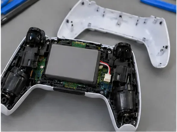 A tampa traseira foi removida de um controle DualSense aberto, com a bateria ainda encaixada.