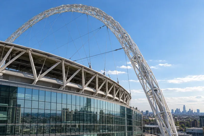 Close architectural view of Wembley Stadium’s tall white arch above the roofline on a clear day