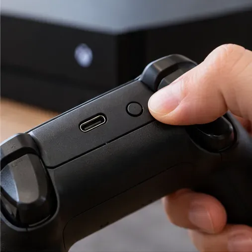 Close-up of a finger pressing the small Pair button beside the USB-C port on a wireless controller